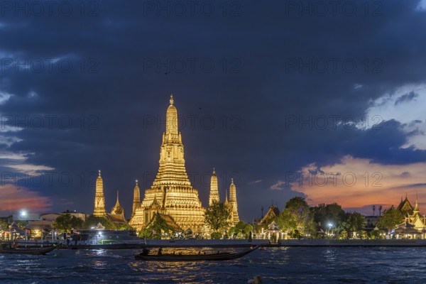 Wat Arun, Temple of Dawn at sunset with dark clouds. Boats on the Chao Phraya river. Tourist