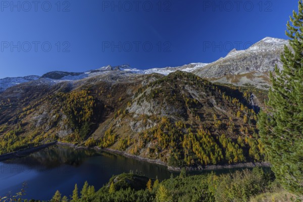 The Galgenbichl reservoir with a mountain forest in fall foliage on a bright sunny morning. Seen