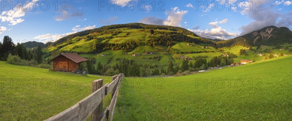 View along a wooden fence across a pasture to the mountains in the evening light, Dolomites, Odle