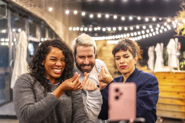 Multiracial diverse friends streaming online with a smartphone and gesturing love during night