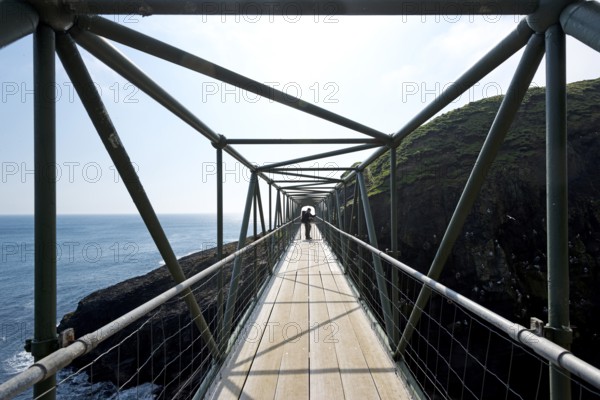 Hiker standing on the so-called Atlantic Bridge, footbridge over a crevice Hólmgjógv, Mykines,