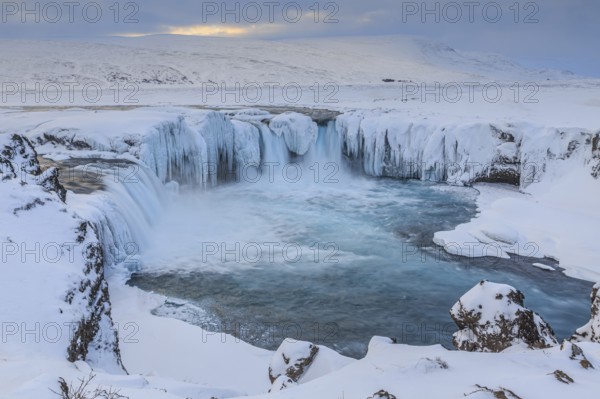 Icy waterfall and rapids in front of a mountain landscape, cloudy mood, snow, Godafoss, Iceland,