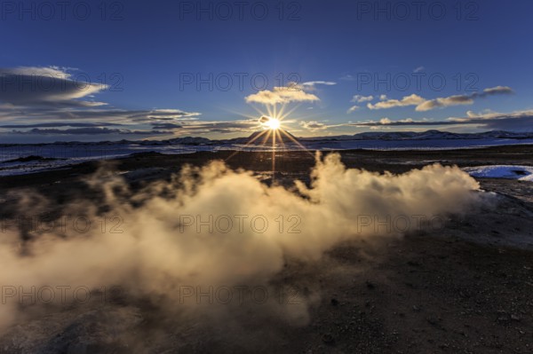 Hot springs and geothermal area in front of mountain landscape in winter, sunbeams, cloudy mood,