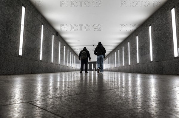 Two men walking through the tunnel subway illuminated with LED light to the underground station
