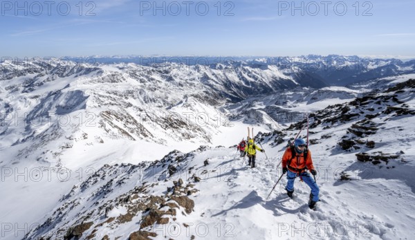 Ski tourer on foot, carrying skis on backpack, mountain panorama, snow-covered mountain landscape
