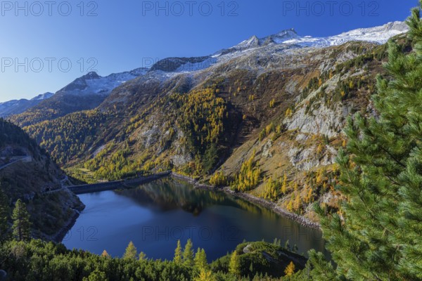 The Galgenbichl reservoir with a mountain forest in fall foliage on a bright sunny morning. Seen