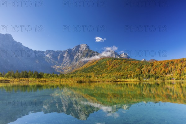 Lake Almsee in autumn with a forest reflected in the lake. A slowly dissipating fog moves over the