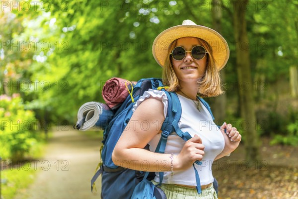 Cheerful caucasian young woman wearing sunglasses and sun hat carrying backpack walking along a