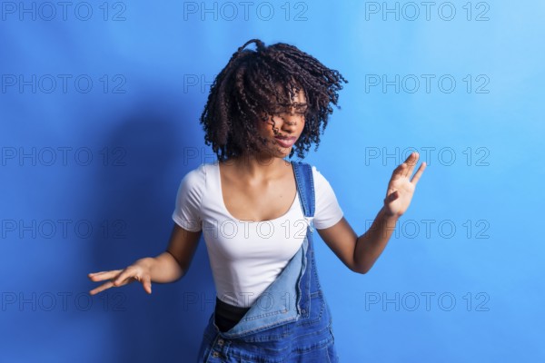Young woman wearing casual clothes dancing with joy and moving her curly hair on a vibrant blue