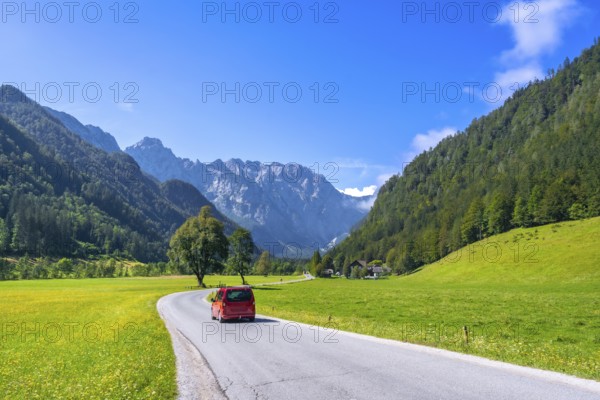 Red van driving along a winding road in the picturesque logarska dolina valley, surrounded by lush