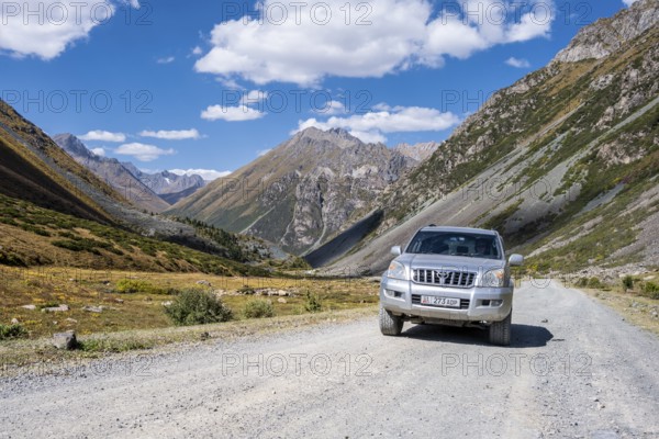Off-road vehicle on a gravel track, picturesque mountain valley, mountain landscape with white