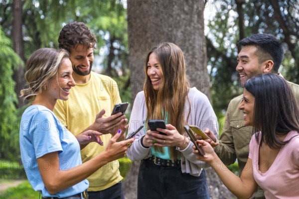 Smiling multiethnic group with phones watching internet or social networks in the park, technology