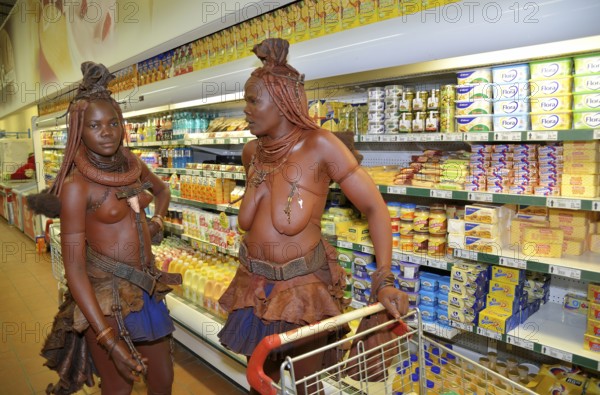 Traditionally dressed Himba women standing in front of the refrigerated section of a supermarket,