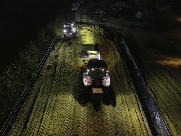 Two tractors filling and levelling a silo at night, maize harvest, Dachtel, Black Forest, Germany,