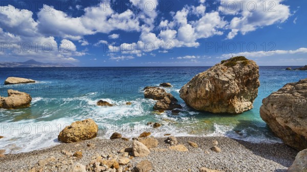 Stony beach with large rocks and gentle waves under a blue sky, Kato Lakkos Beach, still almost
