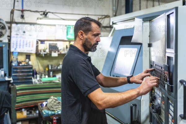 Mature man working on control panel of a lathe in cnc factory
