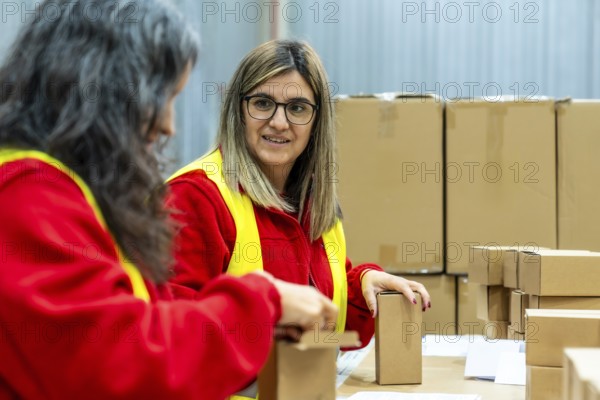 Two adult caucasian women talking relaxed while working in a distribution warehouse preparing boxes