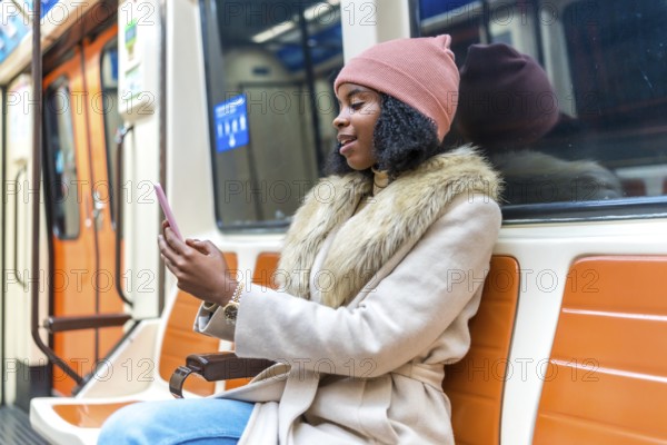 Stylish young woman commuting on a subway train, using her smartphone to browse social media and