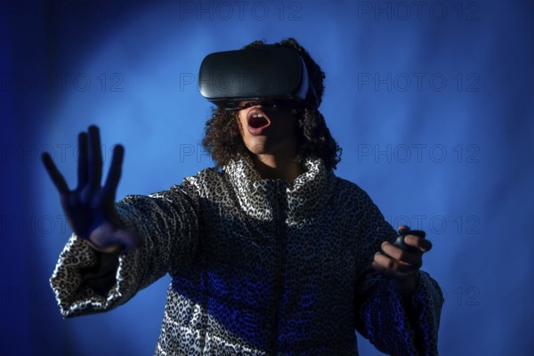 Excited young woman wearing vr headset and using controllers is experiencing metaverse on blue