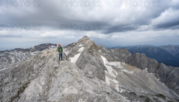 Mountaineer with helmet on a narrow rocky ridge, crossing the Jubiläumsgrat, behind the summit of