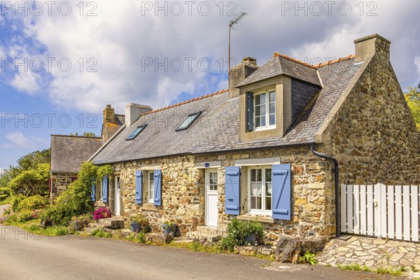 Idyllic old stone cottage by a road in the French countryside with flower pots by the wall on a