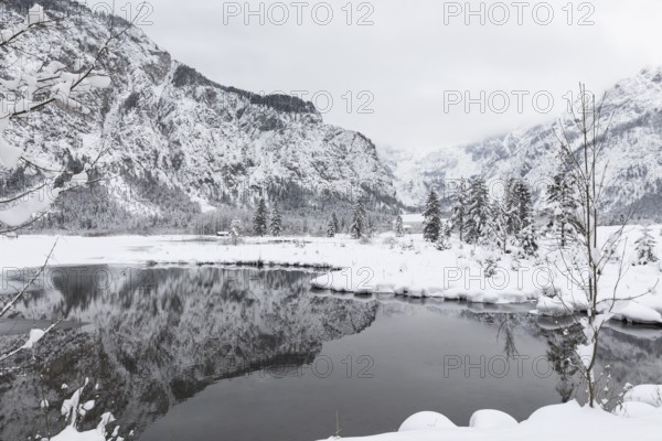 Snow covered Lake Almsee which is partly frozen and snow covered. Snow on the trees and mountains
