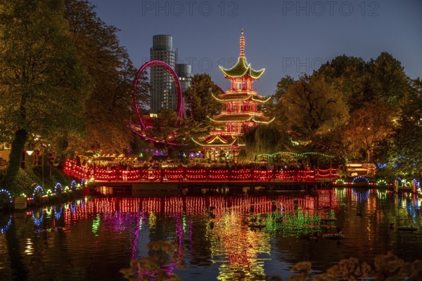Illuminated pagoda, colourful lighting, roller coaster, trees, cityscape at night with modern