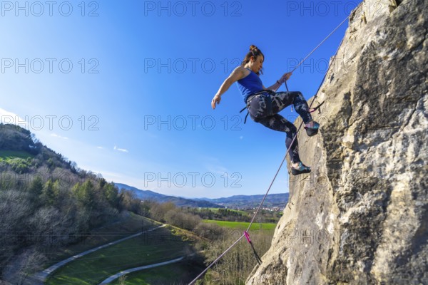 Female climber ascending a rock face, enjoying a sunny day and the beautiful view of the valley