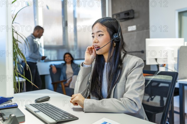 Young asian operator talking with headset and working on computer in a coworking office, with