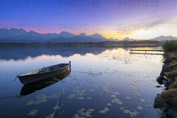 Boats at a jetty on a calm lake at sunset with mountains in the background, Hopfensee, Hopfen am