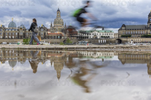 The Dresden silhouette with a cyclist and dark clouds behind the Church of Our Lady is reflected in