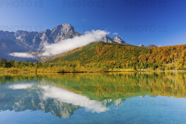 Lake Almsee in autumn with a forest reflected in the lake. A slowly dissipating fog moves over the