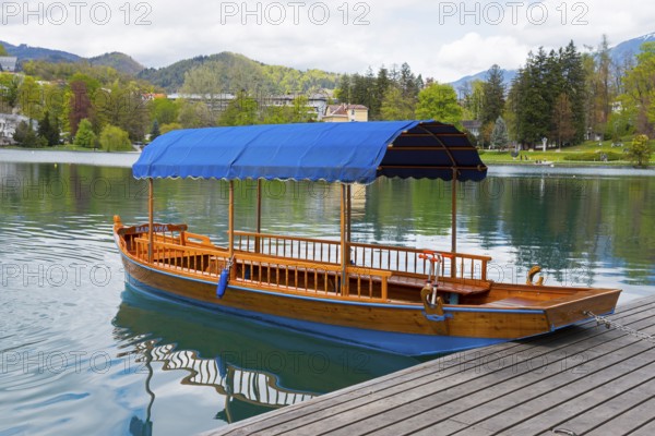 A single wooden boat with a blue roof lies on a platform in a calm lake, Lake Bled, Lake Veldes,