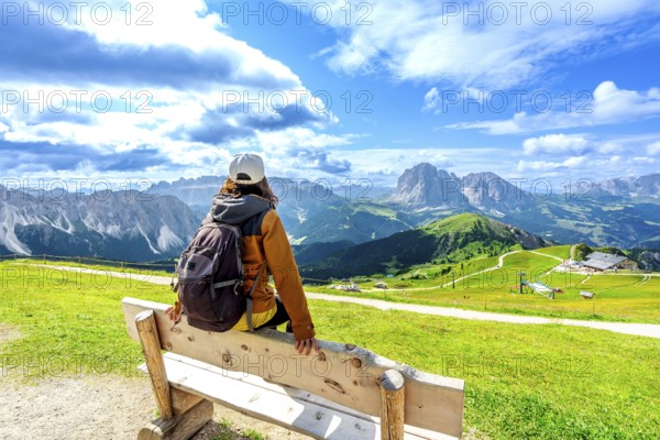 Hiker resting on a wooden bench admiring the beautiful mountain landscape of seceda in the italian