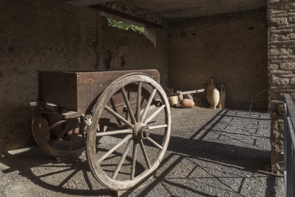 Old wooden cart and ceramic jugs on display inside an unenclosed building at the ancient ruins of