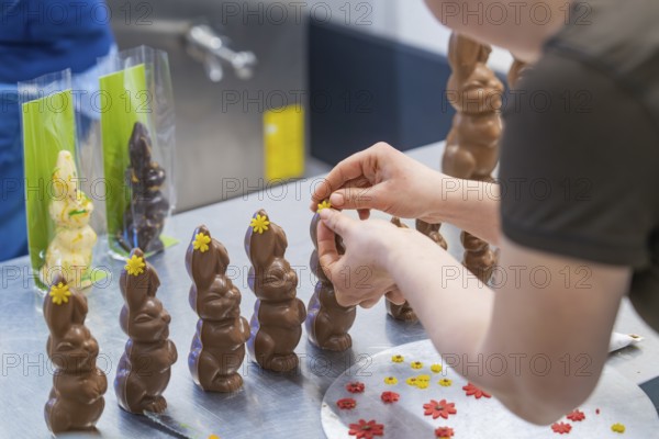 Person decorating several chocolate bunnies with flowers on a work table, Easter baking and