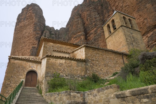 Historic church with bell tower and stone walls, situated at the foot of steep mountains, Las Peñas