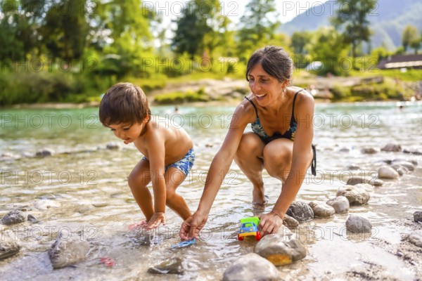 Mother and son enjoying summer holidays, playing with toy cars in the refreshing water of lake