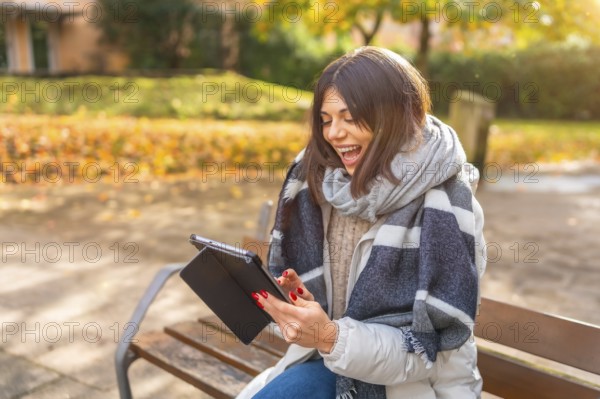 Rays of the sun illuminating a caucasian happy woman laughing while using digital tablet in a park