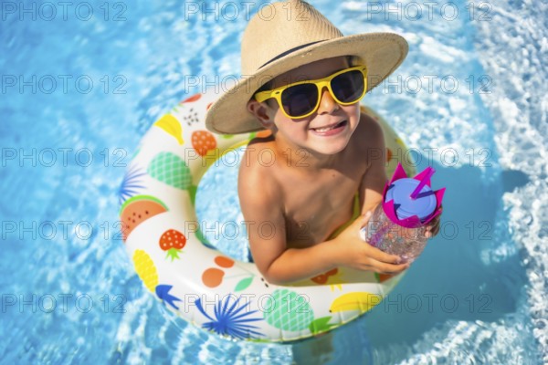 Top view close-up of a funny caucasian boy inside a pool drinking water into a rubber ring colorful