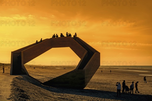 Westerpunt silhouetted against orange sunset sky, concrete sculpture on beach along North Sea coast