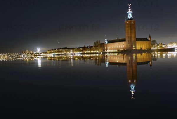 Illuminated building by a calm body of water at night with reflecting water and dark sky, capital