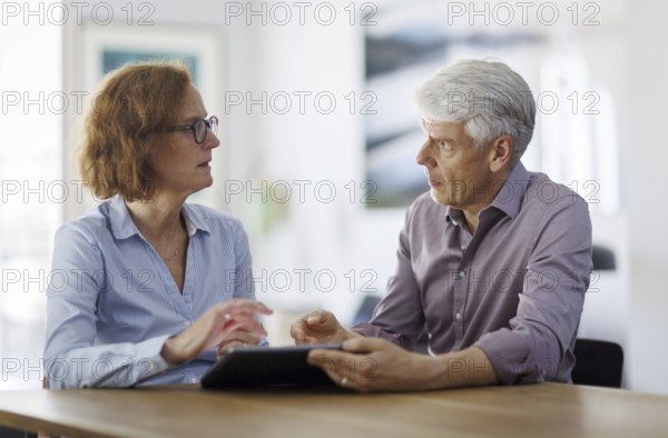 Symbolic photo. A woman and a man sit together at a table with a tablet and talk. Berlin, 13.08