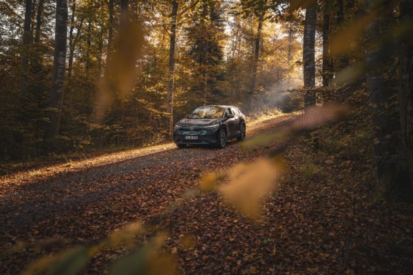 Car driving slowly through a quiet, autumnal forest path in the sunlight, electric car VW ID5,