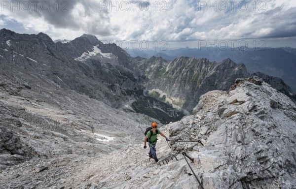 Mountaineer with helmet climbing on rock, on a narrow rocky ridge, view of Zugspitze and Höllental