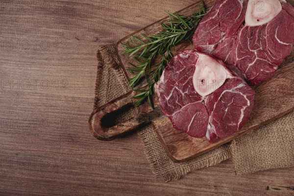 Knuckle on the bone, raw meat for ossobuco, on a wooden chopping board, with a sprig of rosemary,