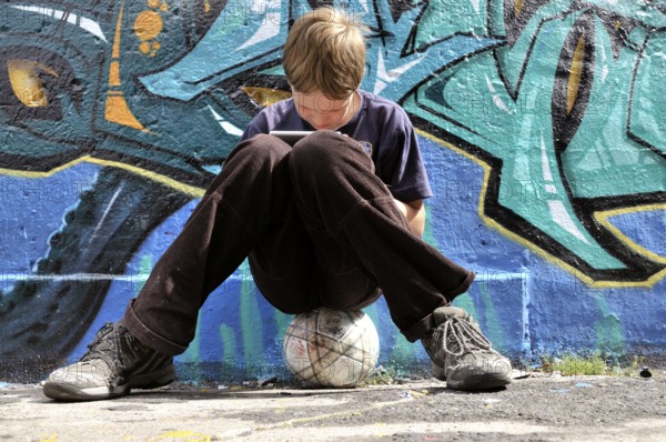 Ten-year-old boy playing with his Nintendo in front of a graffiti wall, football pitch, Germany,