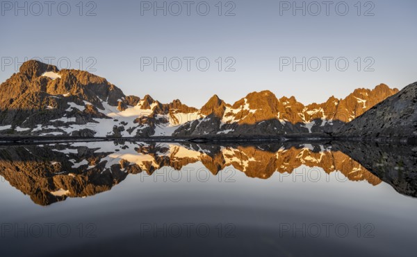 Rocky mountain peaks reflected in a small pond, mountain landscape with alpenglow at sunrise, at