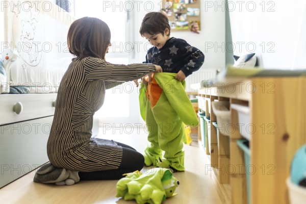 Mother assisting her son in putting on a colorful dinosaur costume, enjoying playful moments