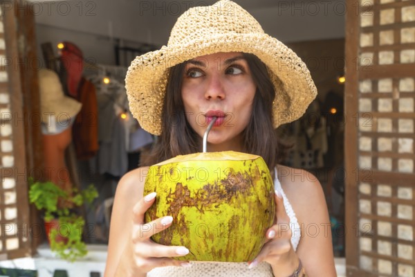 Young woman wearing straw hat enjoying refreshing coconut water during tropical vacation in siargao